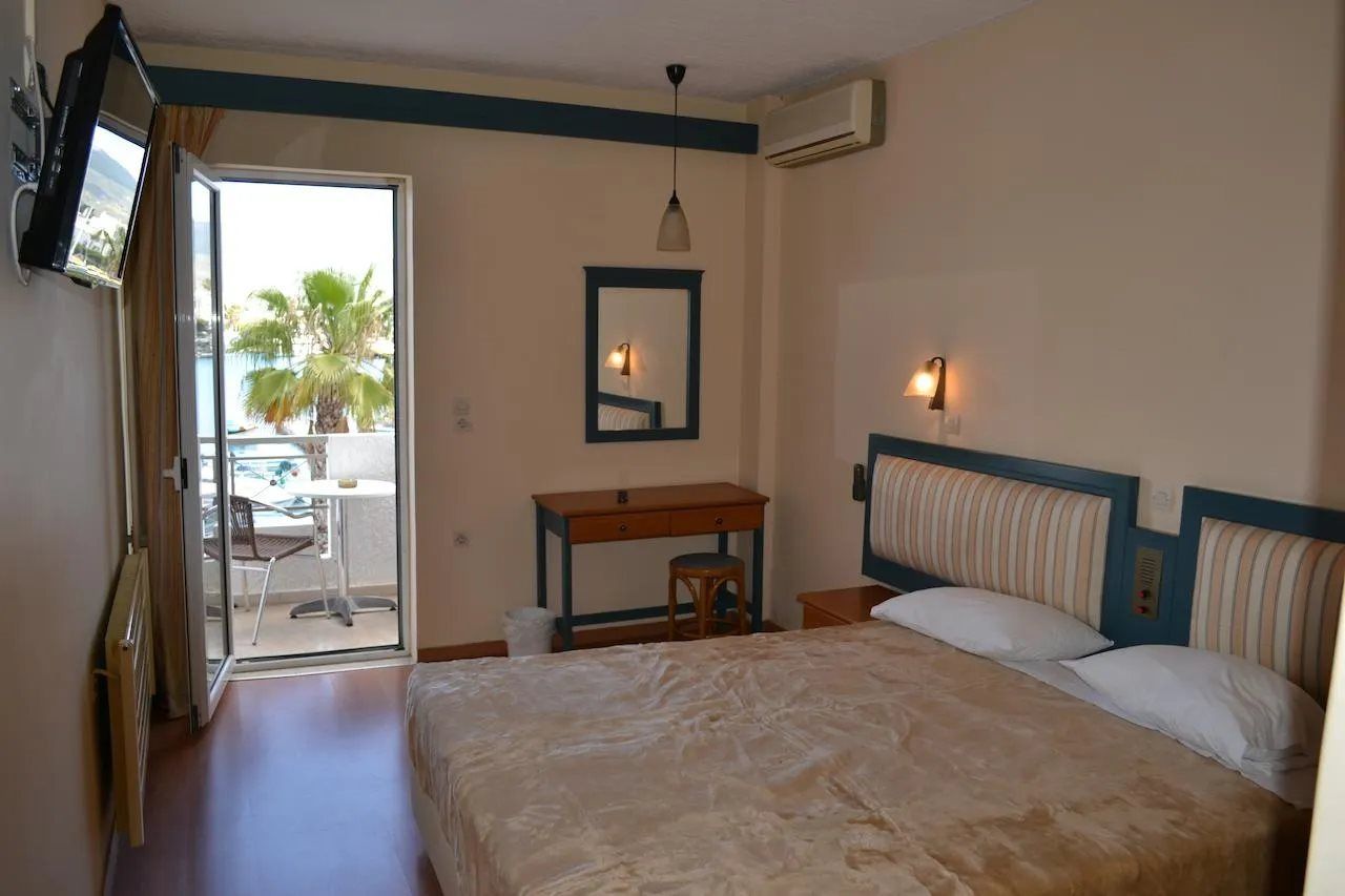 Une chambre d’hôtel équipée d’un lit, d’un bureau, d’une chaise, d’une petite table, d’un miroir et d’un balcon offrant une vue sur les palmiers.