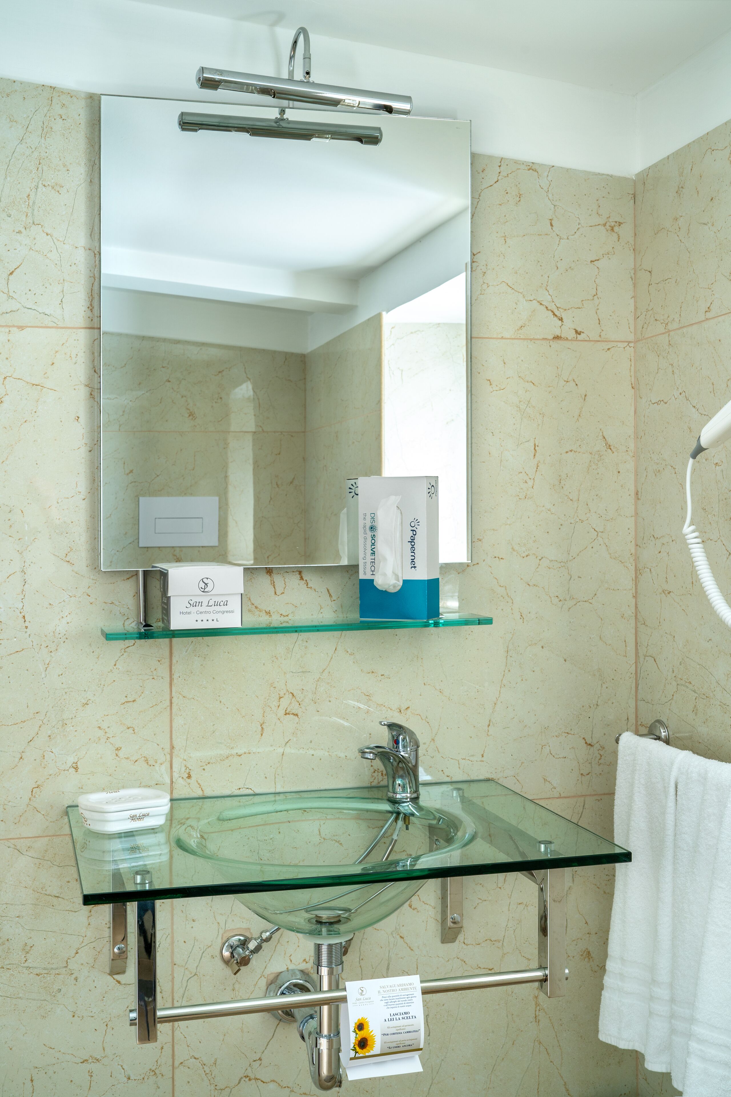 Un baño con lavamanos de vidrio, un espejo, toallero y secador de pelo.