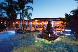 A resort with a clear pool, palm trees, and a building with outdoor seating. - Hotel San Luca (Battipaglia)