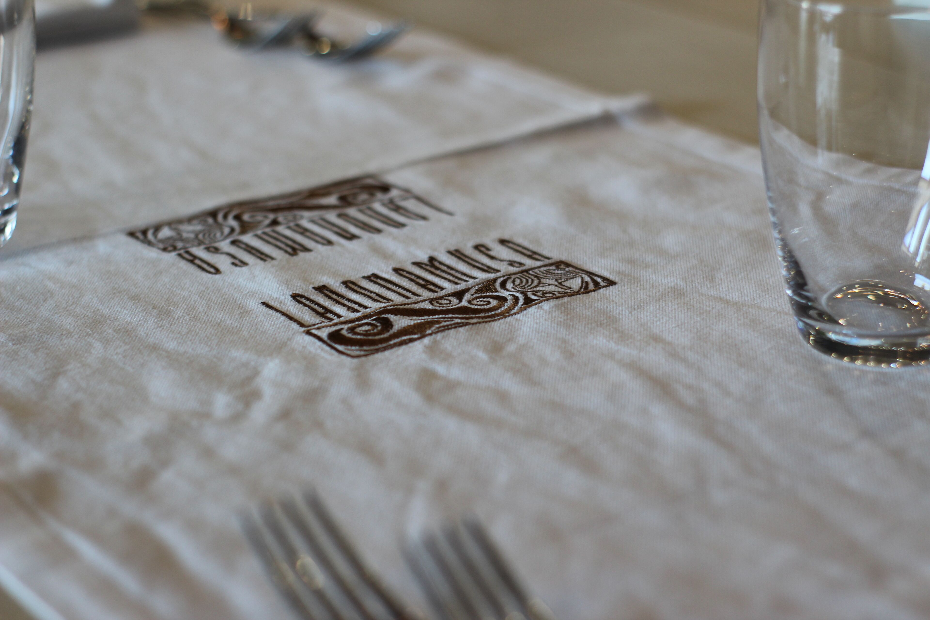 A table with a cloth napkin featuring embroidered text and a glass.