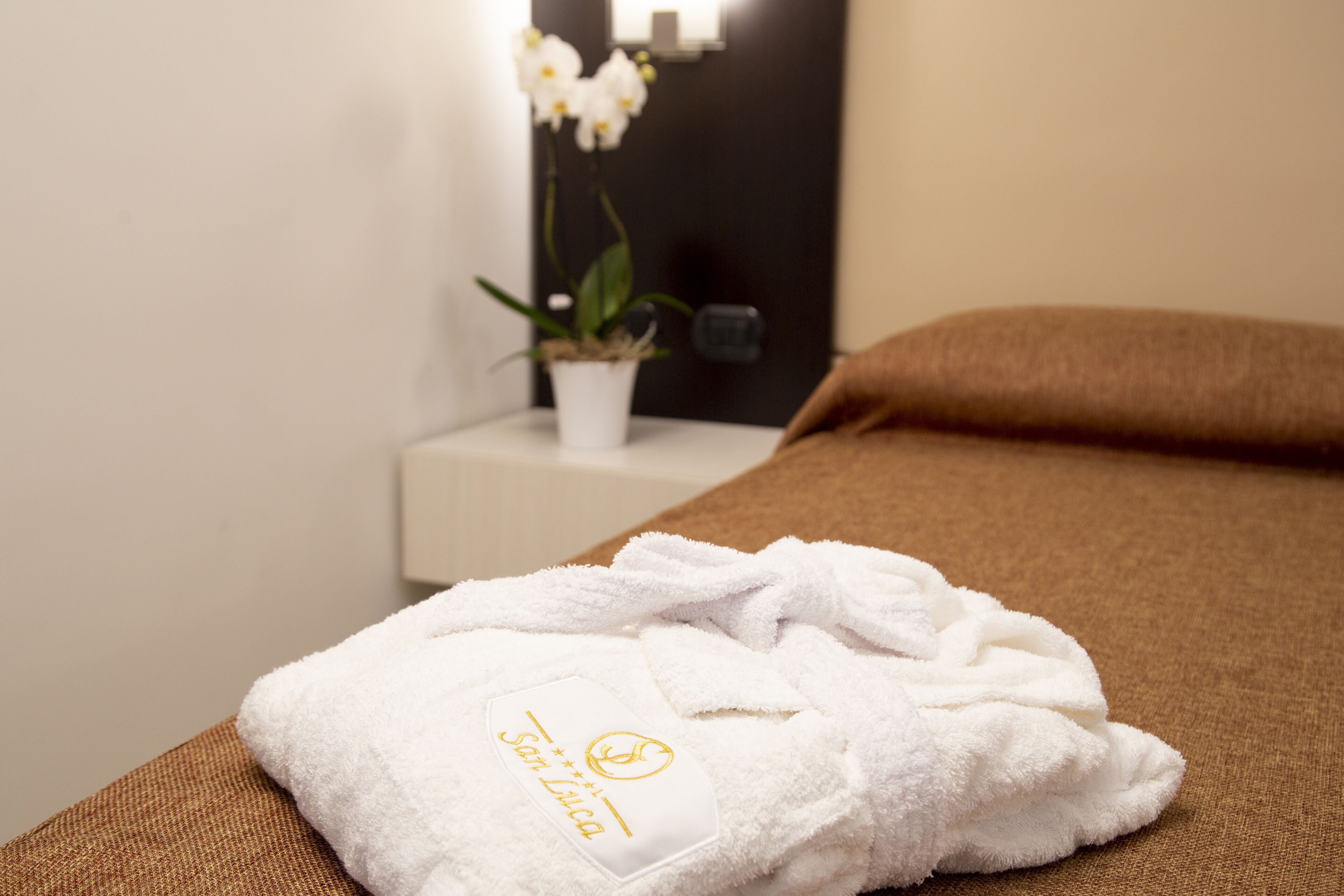 A neatly made bed with a white towel on it, a small potted plant, and a brown pillow.