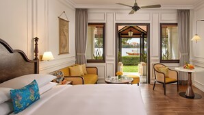 A hotel room with a bed, a sofa, a dining table, and a view of a garden. - Anantara Hoi An Resort (Da Nang)