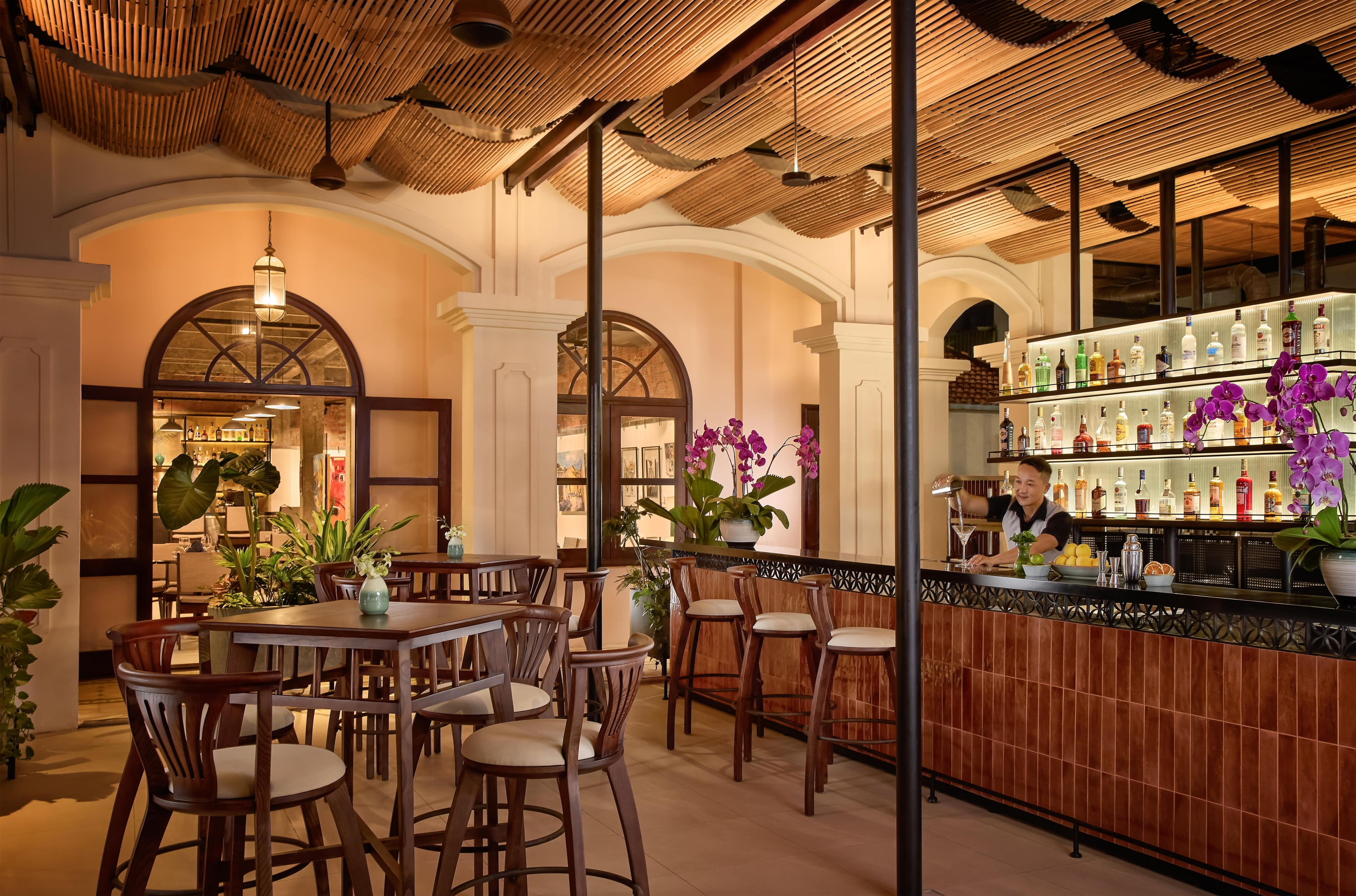 A bar area with wooden furniture, a bartender, and a variety of bottles.