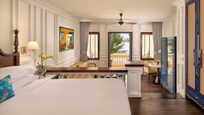 A hotel room with a large bed, a desk, a chair, a television, and a balcony with a view of the water.