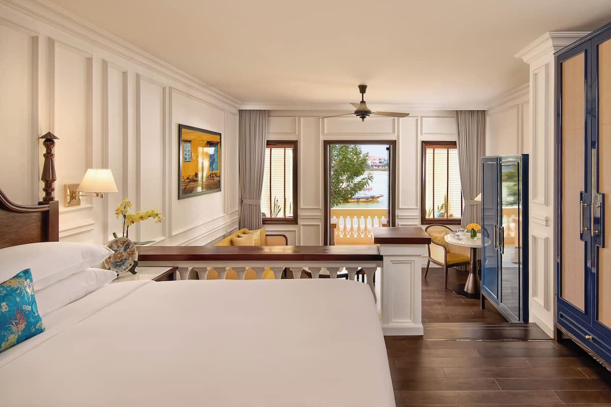 A hotel room with a large bed, a desk, a chair, a television, and a balcony with a view of the water.