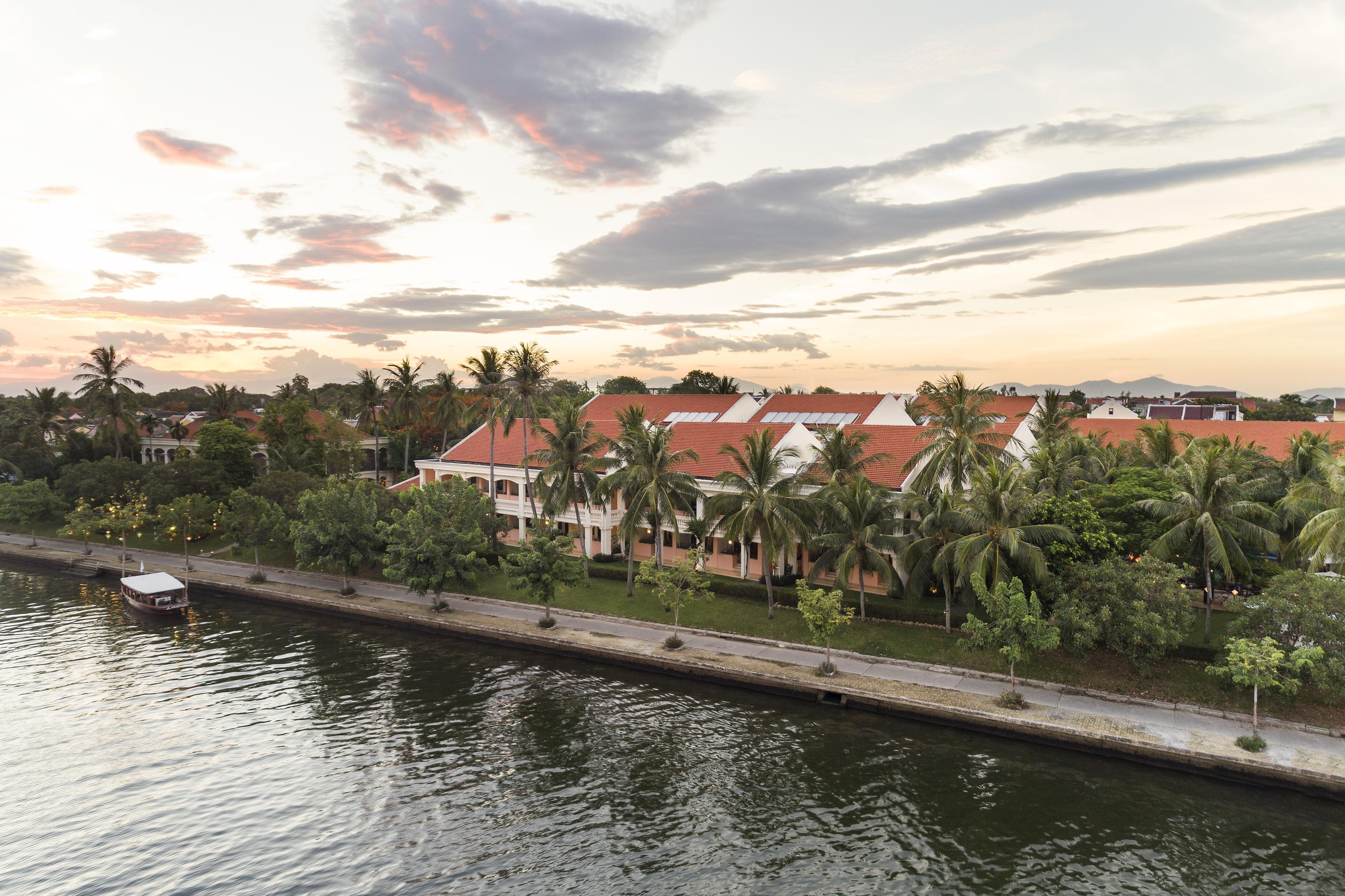 A waterfront hotel with a row of villas, a canal, and palm trees.