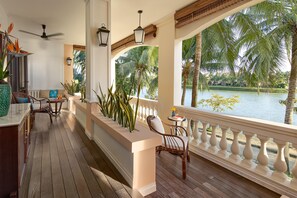 A wooden deck with a railing, a table, chairs, and a view of a lake with palm trees. - Anantara Hoi An Resort (Da Nang)