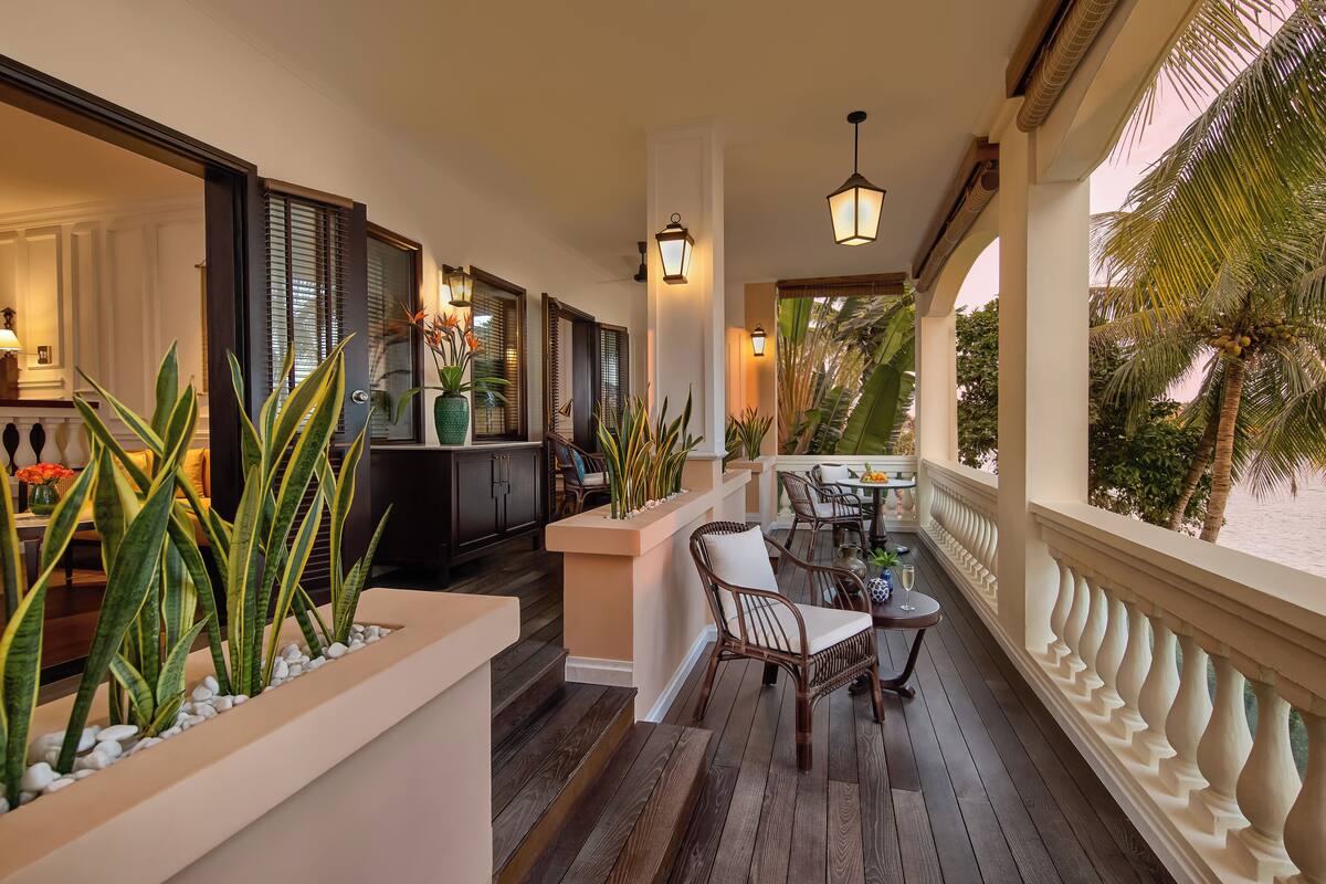 A covered outdoor area with a wooden deck, seating, potted plants, and a view of the beach.