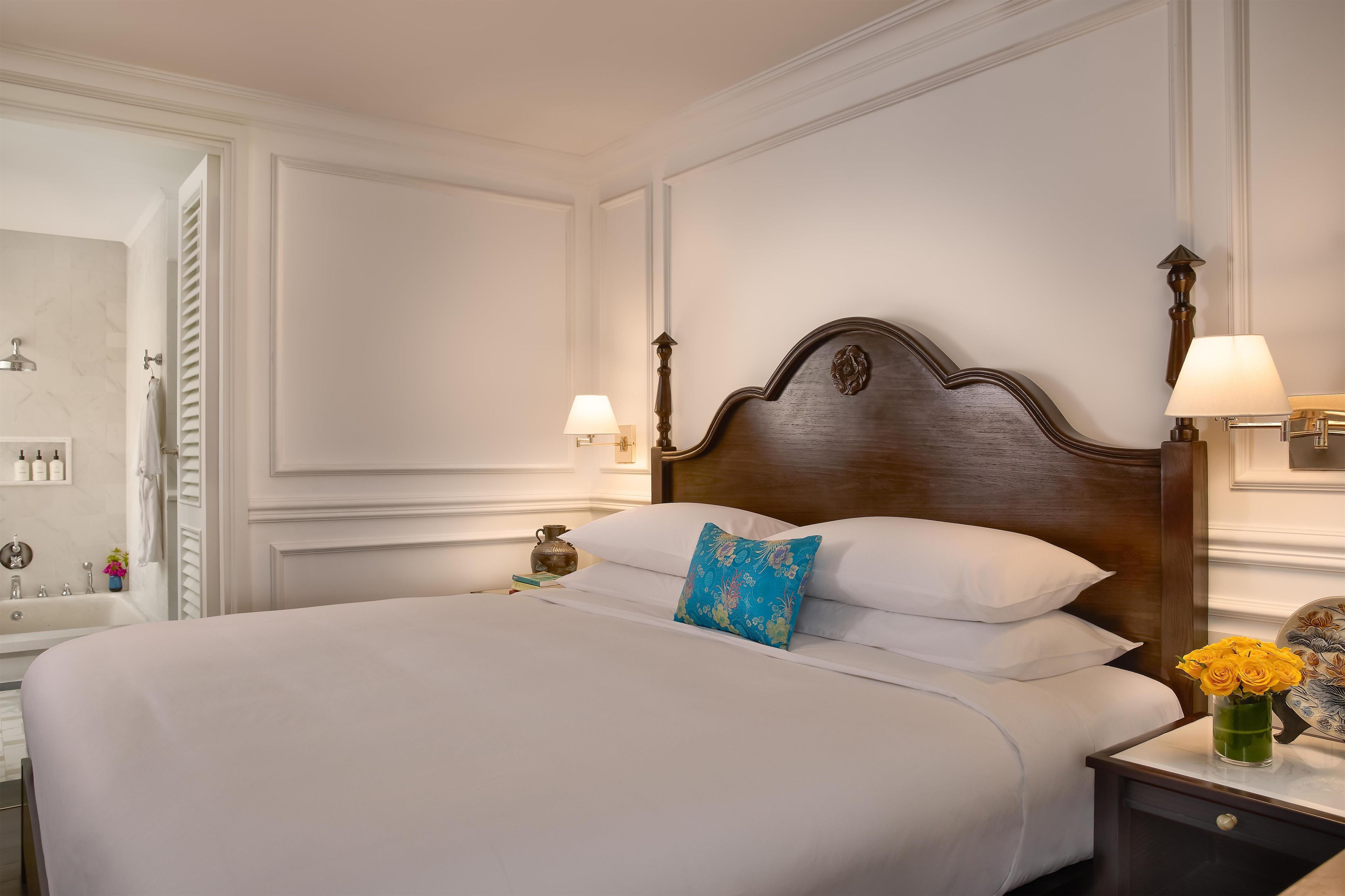 A neatly made bed with white linens, a blue floral pillow, and a vase of yellow flowers on the nightstand.