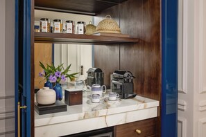 A kitchen counter with a coffee maker, teapot, cups, and jars on a shelf above. - Anantara Hoi An Resort (Da Nang)