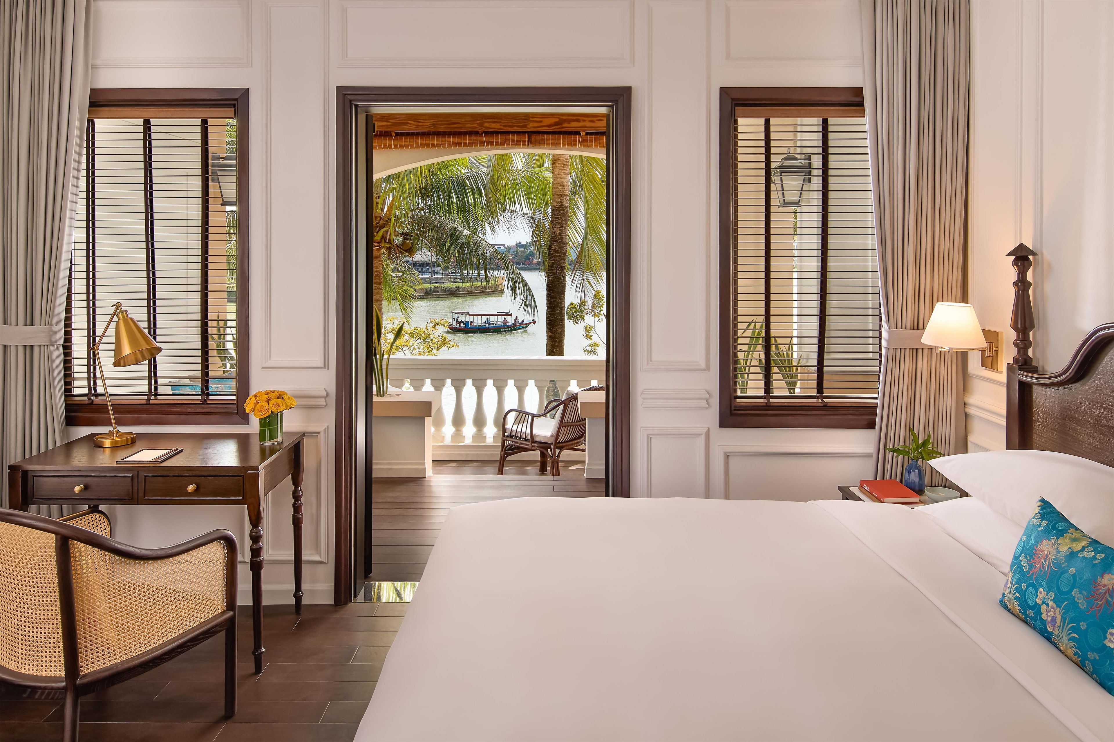 A hotel room with a bed, desk, chair, and a view of a boat on a body of water.