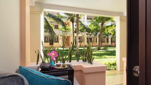 A balcony with a view of a courtyard, a sofa, a small table with decorative items, and a door. - Anantara Hoi An Resort (Da Nang)