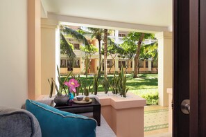A balcony with a view of a courtyard, a sofa, a small table with decorative items, and a door. - Anantara Hoi An Resort (Da Nang)