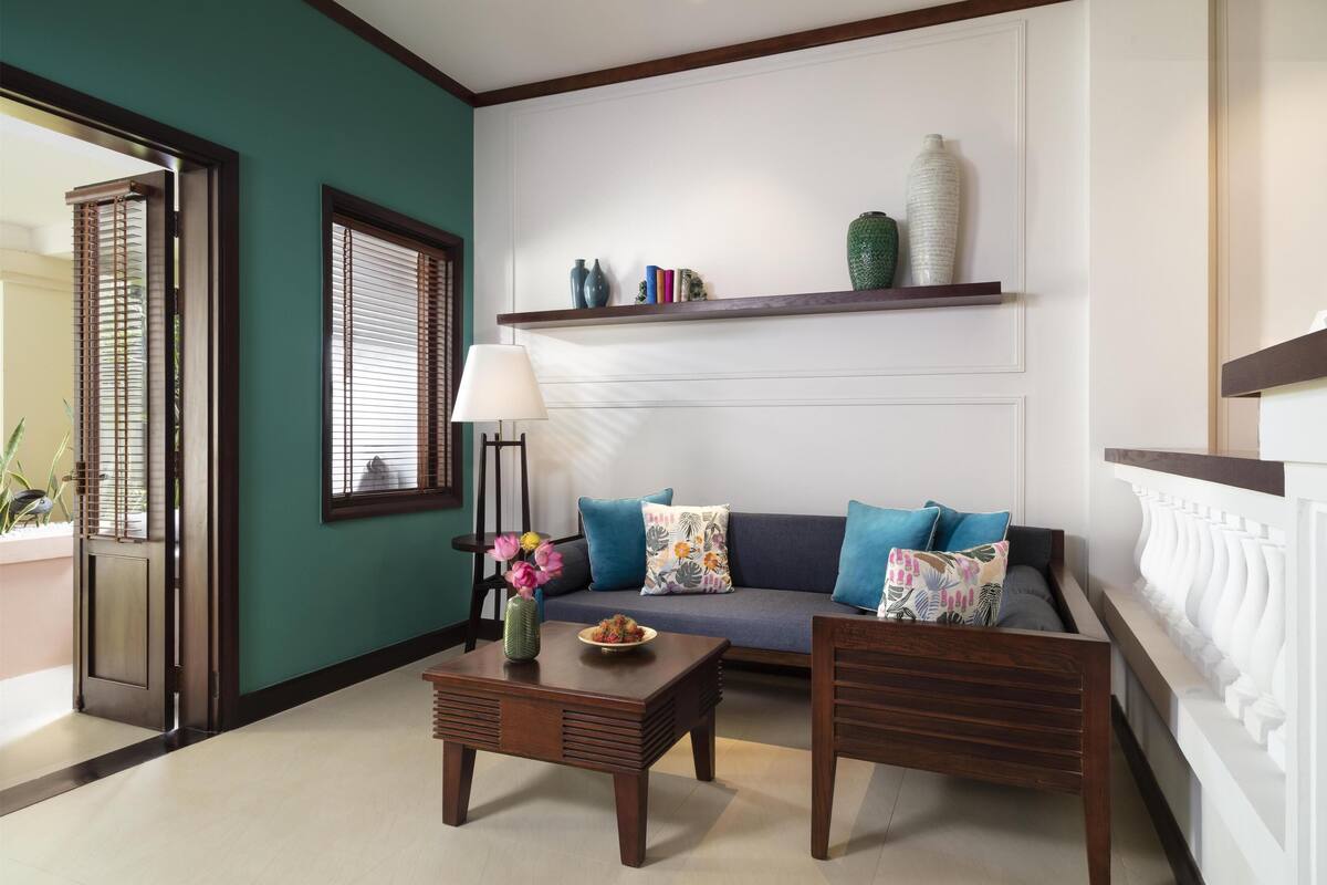 A living room with a sofa, two wooden chairs, a coffee table, a lamp, and a shelf with decorative items.