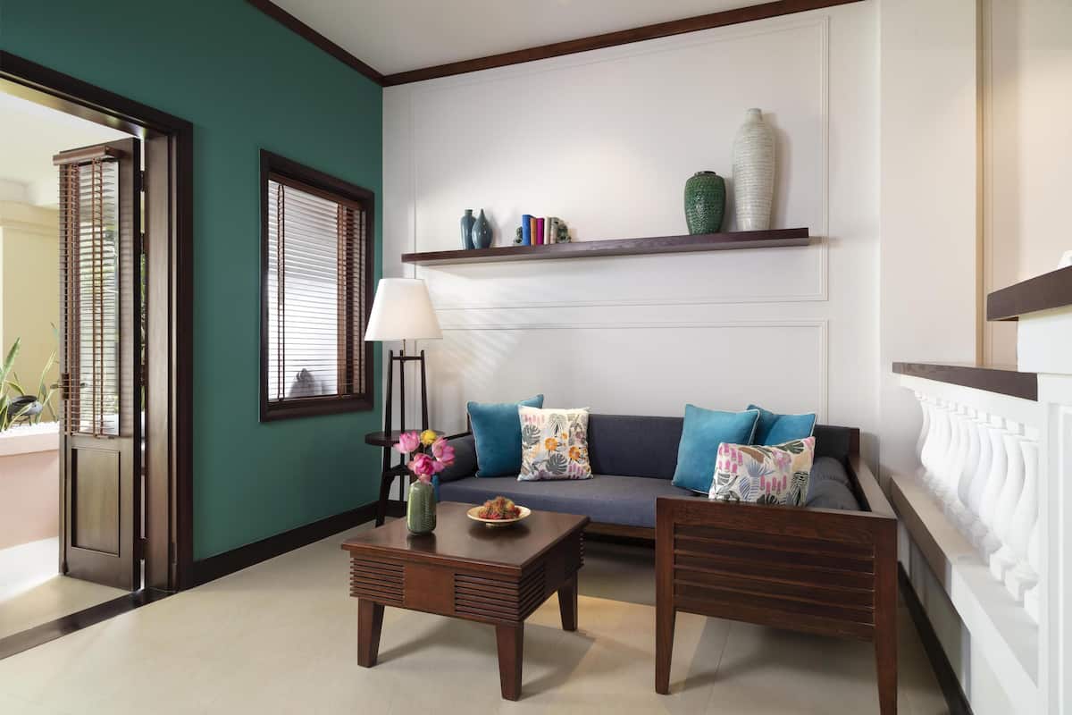 A living room with a sofa, two wooden chairs, a coffee table, a lamp, and a shelf with decorative items.