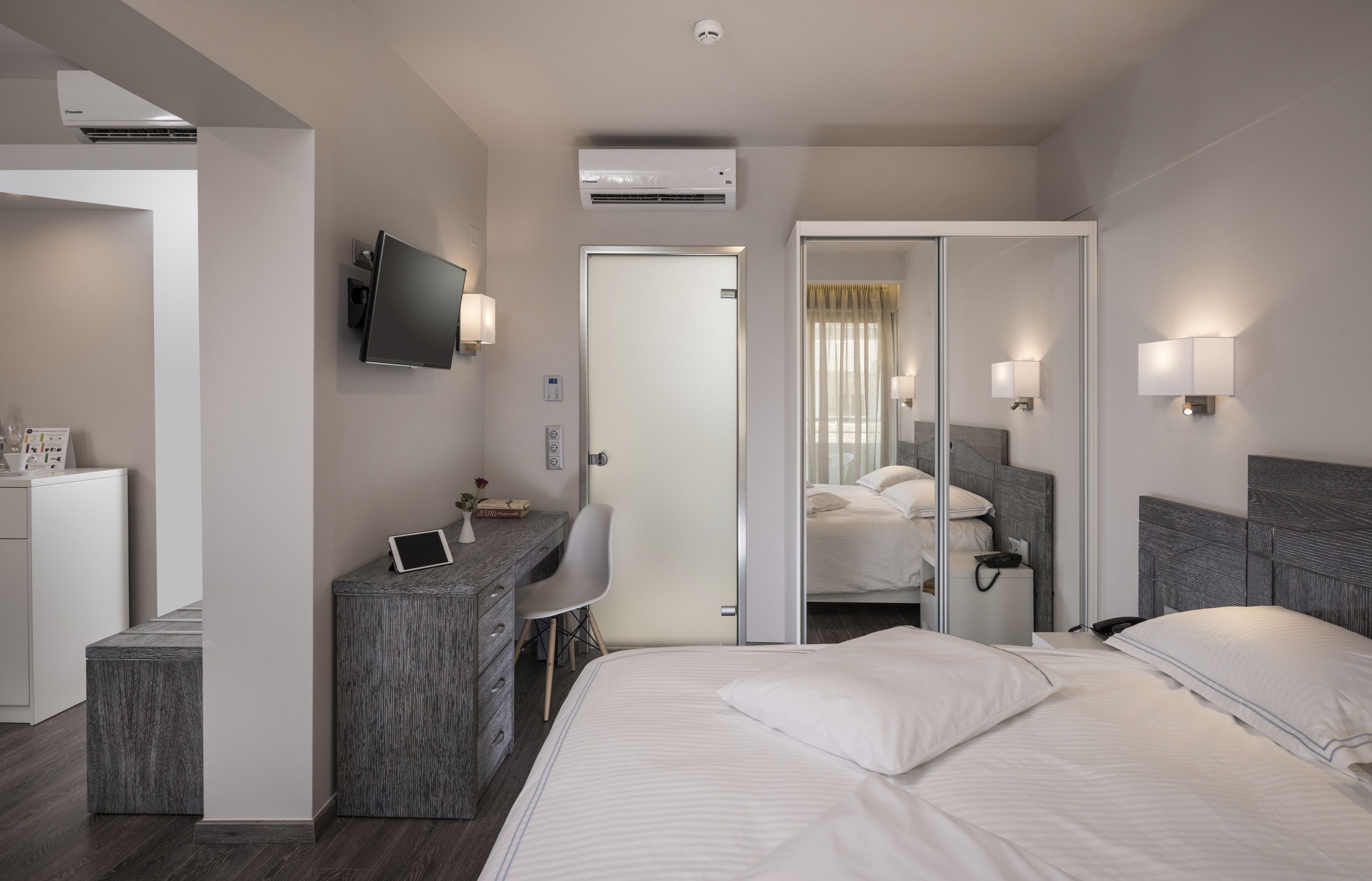 Une chambre d’hôtel moderne équipée d’un lit, d’un bureau, d’une chaise et d’un téléviseur fixé au mur.
