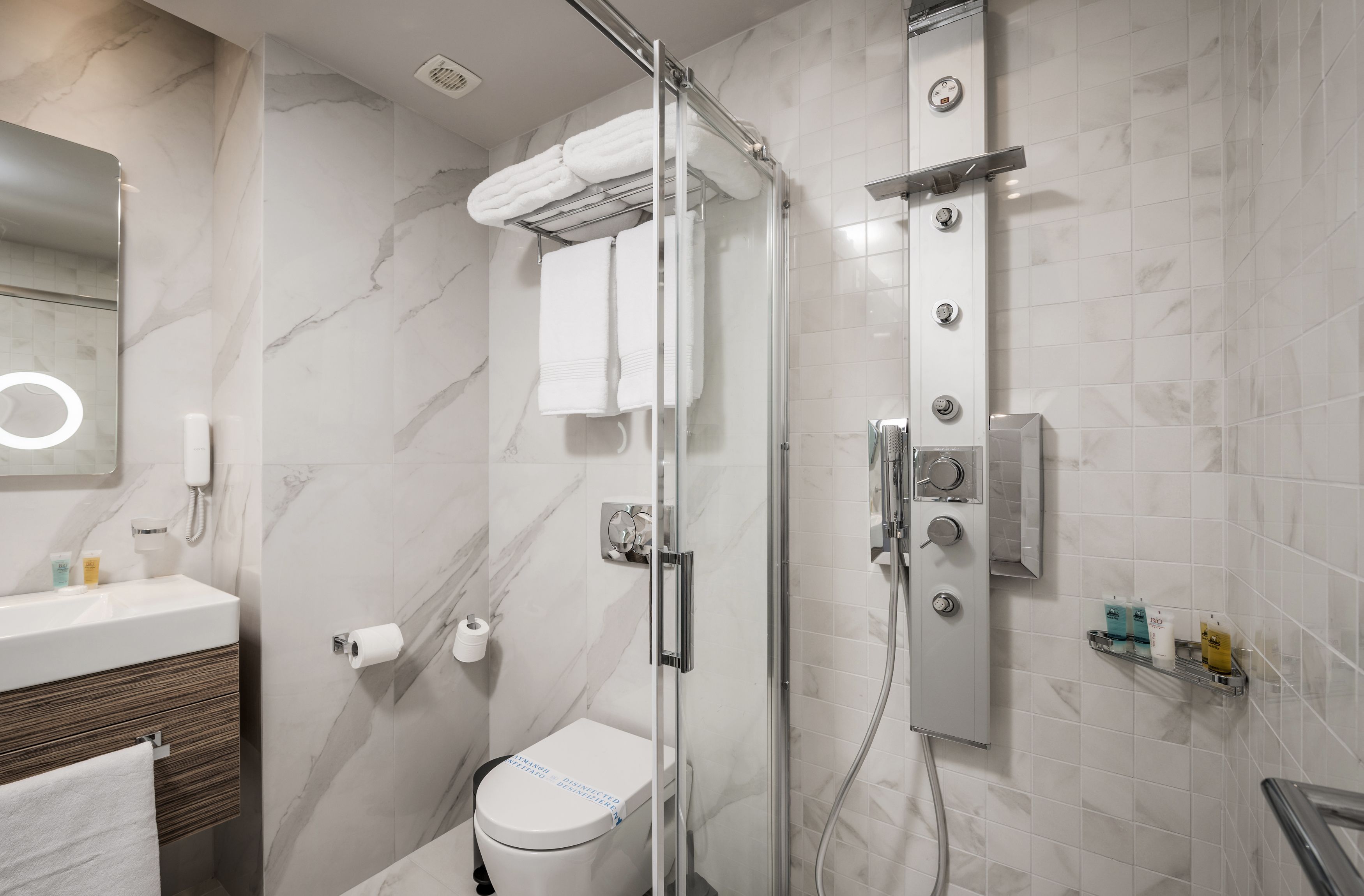 Ein modernes Badezimmer mit einer gläsernen Duschkabine, Toilette und einem Waschtisch mit Spiegel und Handtuchhalter.