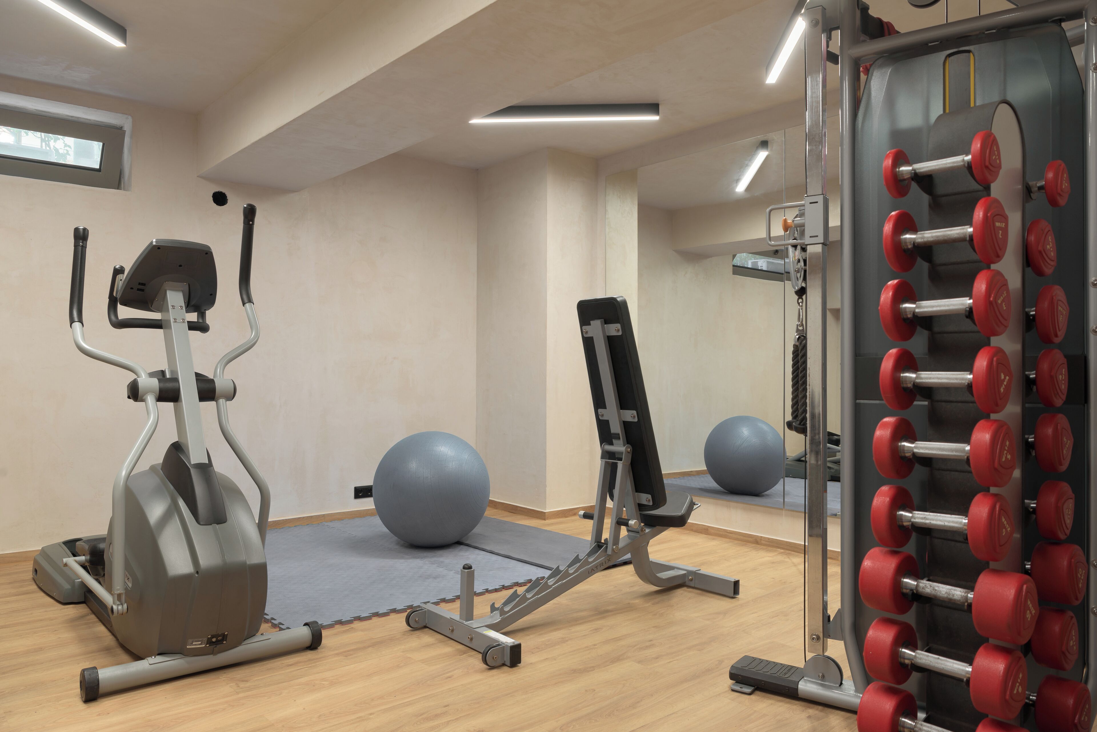 Uma academia com equipamentos de ginástica, incluindo uma elíptica, um banco e uma barra de halteres.