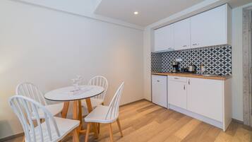 Uma cozinha compacta com armários brancos, backsplash estampado e um pequeno espaço de jantar com mesa redonda e cadeiras brancas.