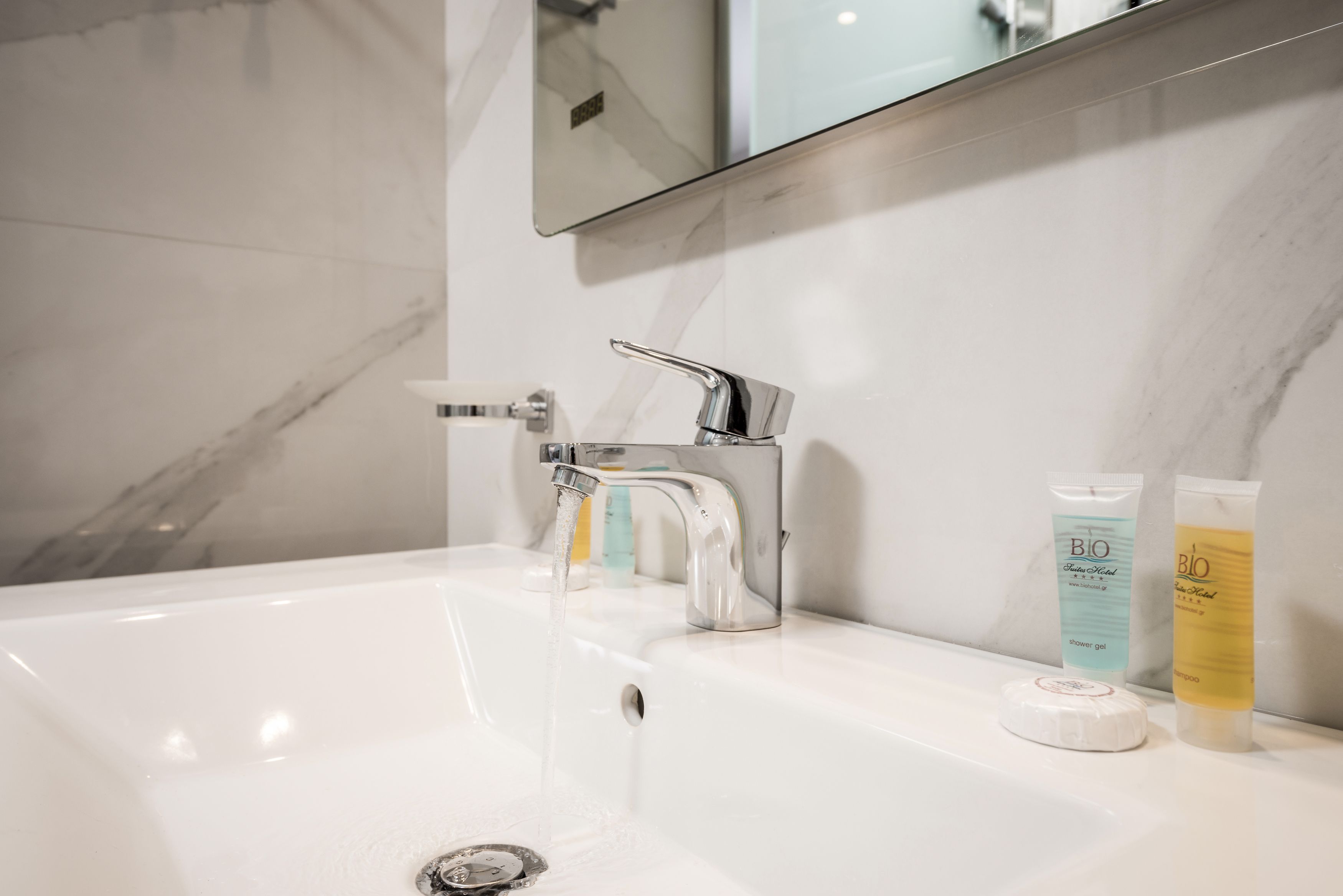 Une salle de bain avec un lavabo blanc, un robinet chromé et deux bouteilles de shampoing et d’après-shampoing.
