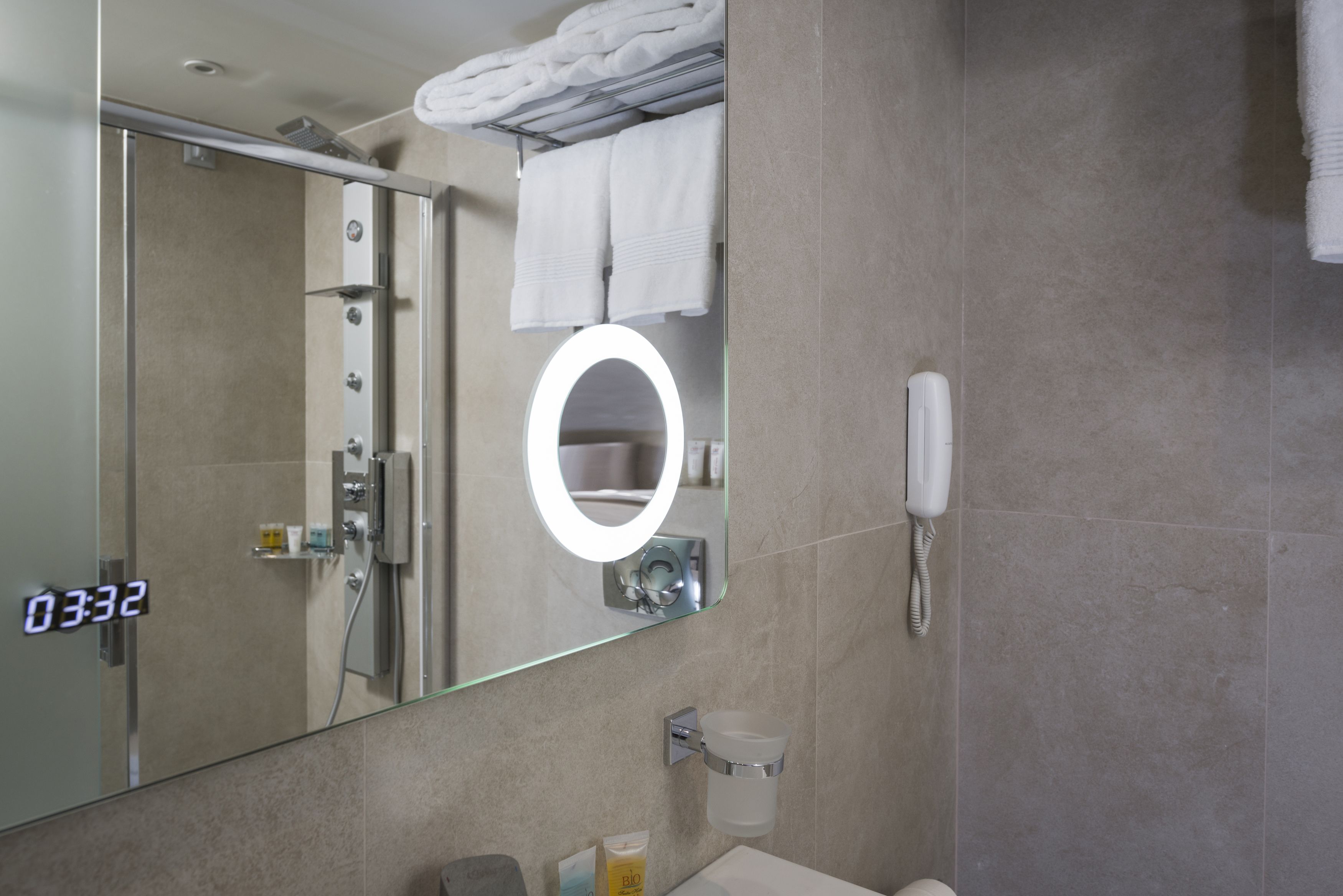 A modern bathroom with a glass-enclosed shower, a vanity with a sink, a mirror with a built-in light, and a telephone.