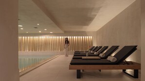 Un área de spa con piscina, sillones reclinables y una persona caminando hacia la piscina.