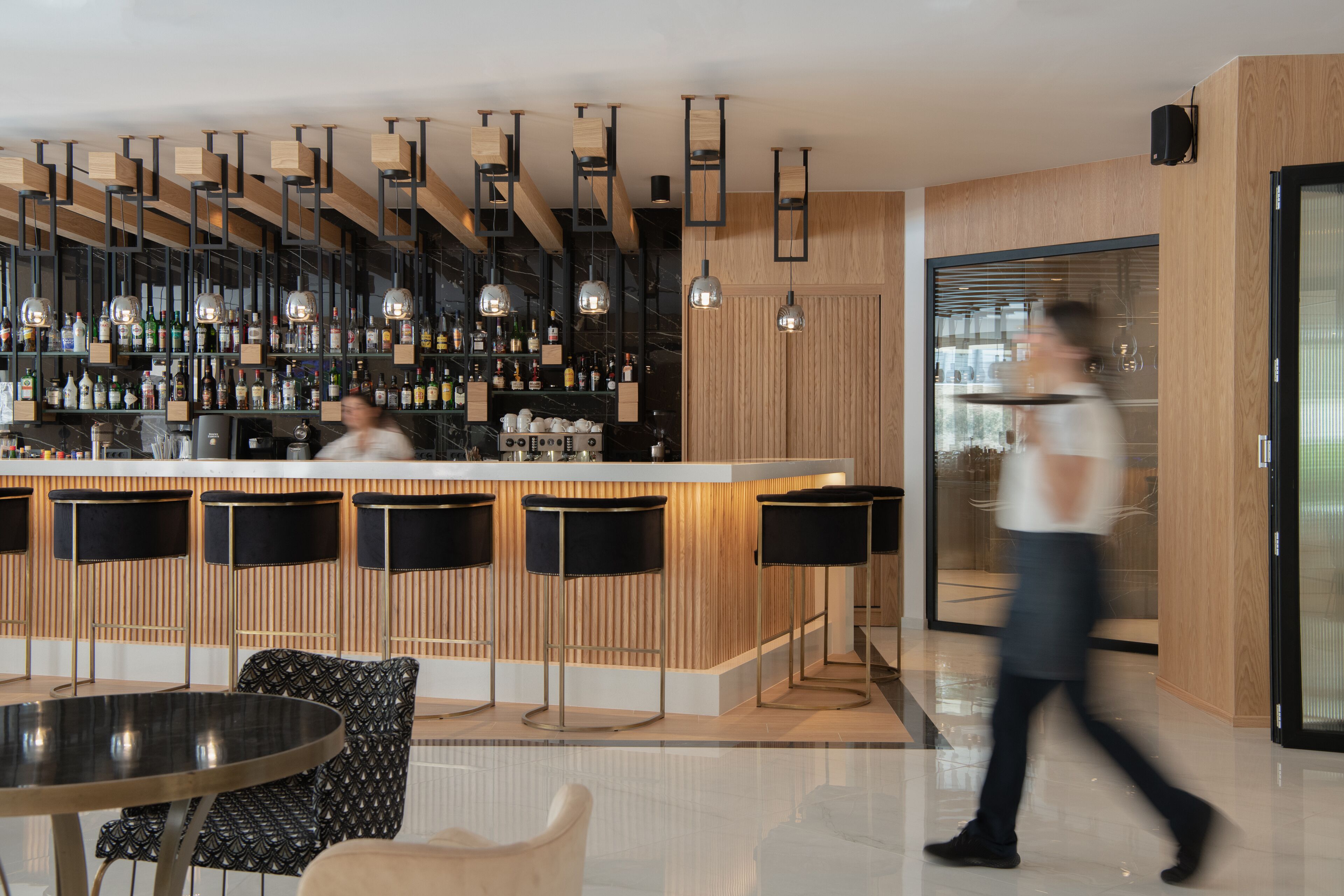 A modern bar area with a bartender, wooden accents, and bar stools.