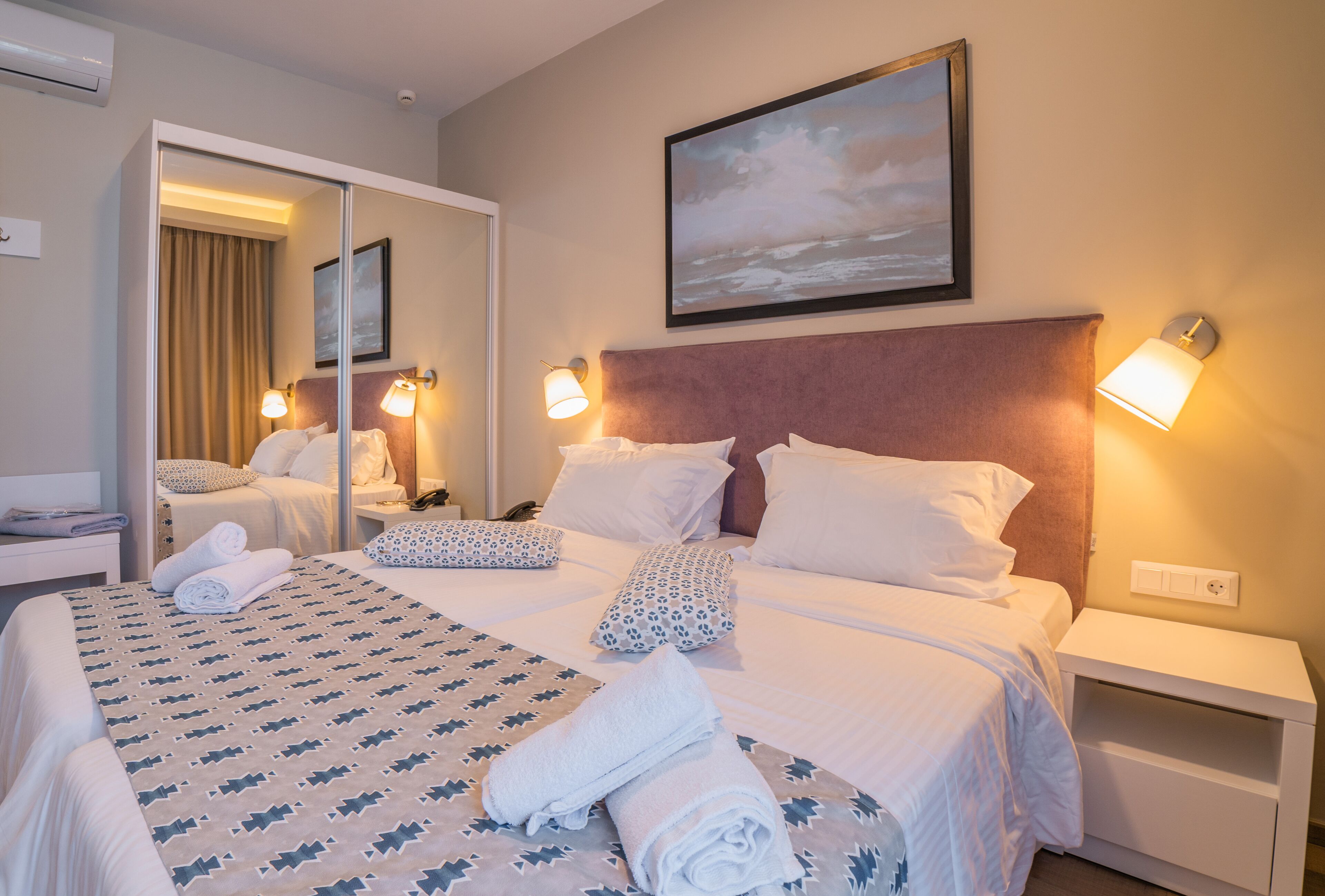 A hotel room with a large bed, two bedside tables, a mirror, and a painting on the wall.