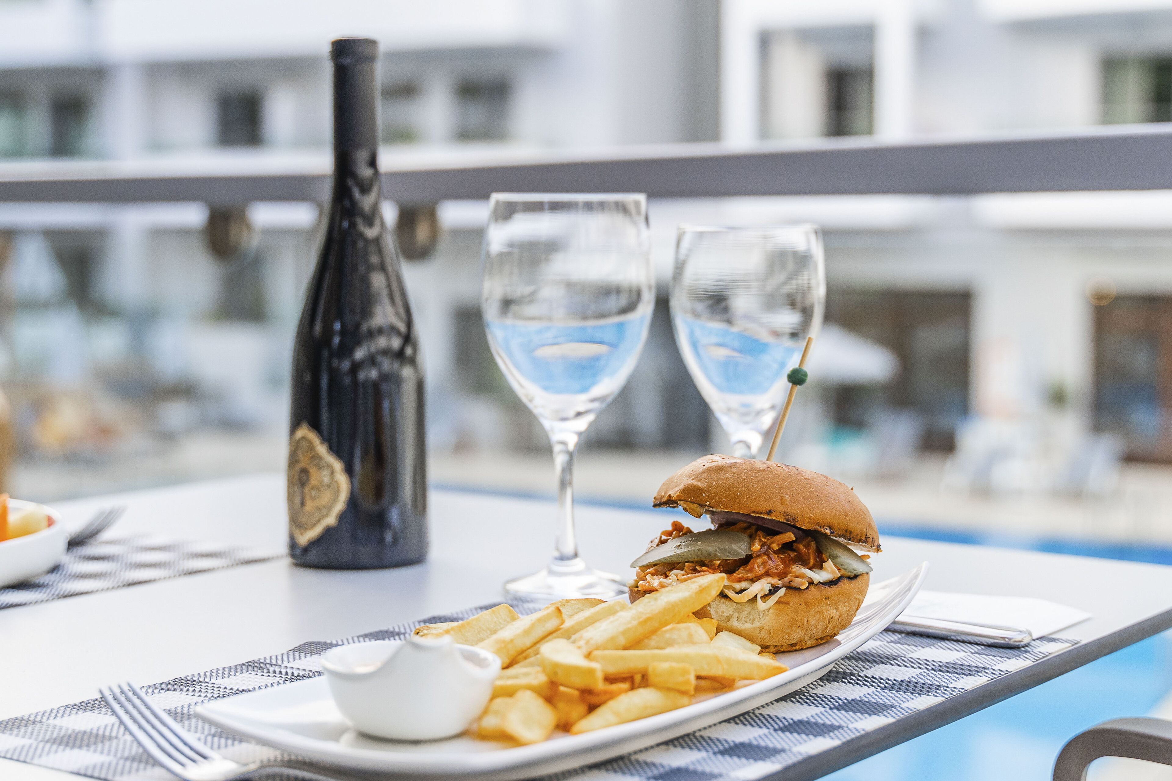 Een eettafel met een bord friet, een hamburger, een fles en twee glazen water.