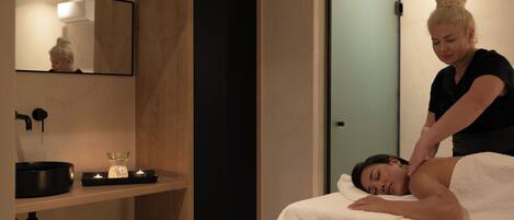 A spa room with a massage table, a mirror, a sink, and a shelf with candles.