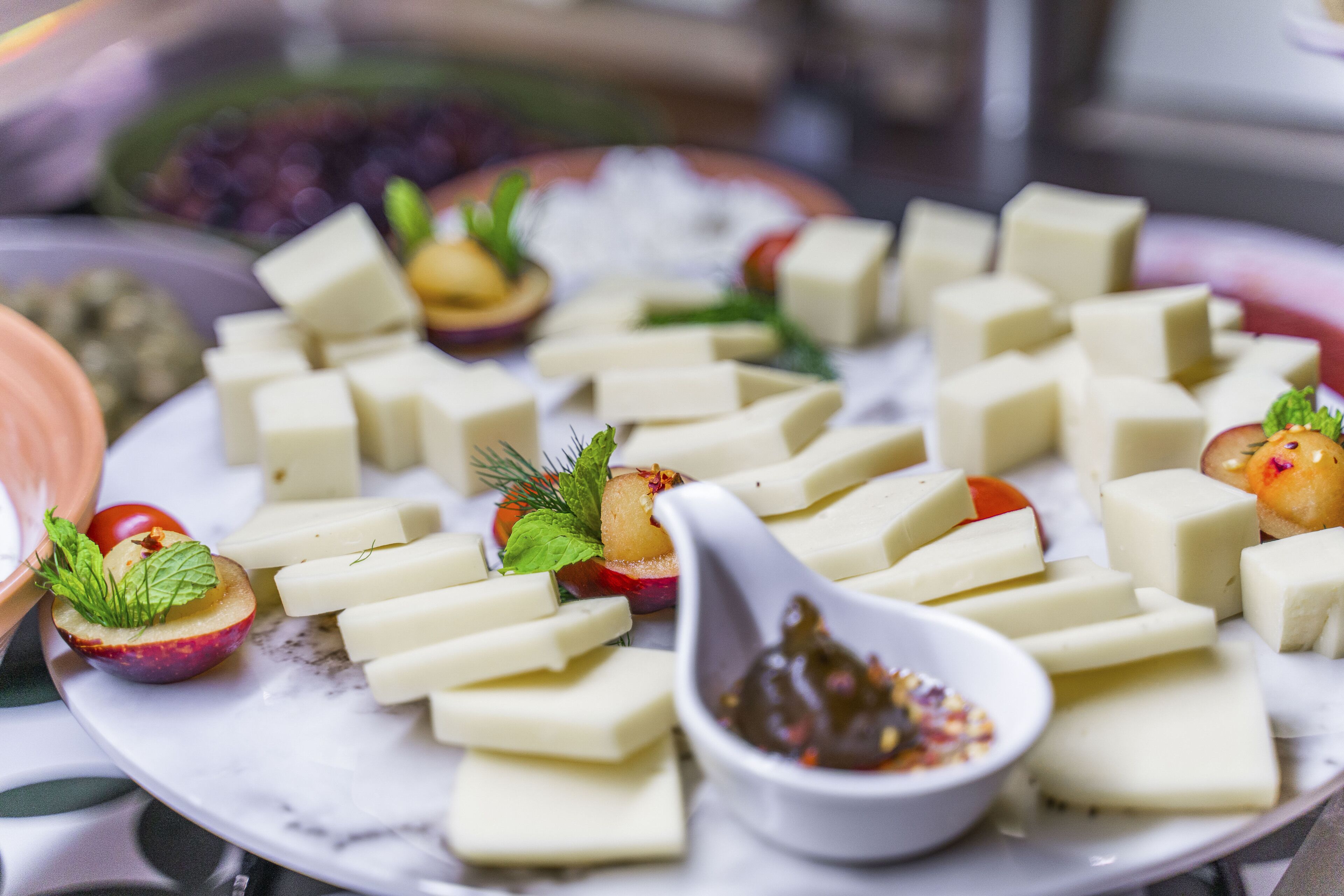 A plate of cheese cubes with garnishes and a small bowl of sauce.