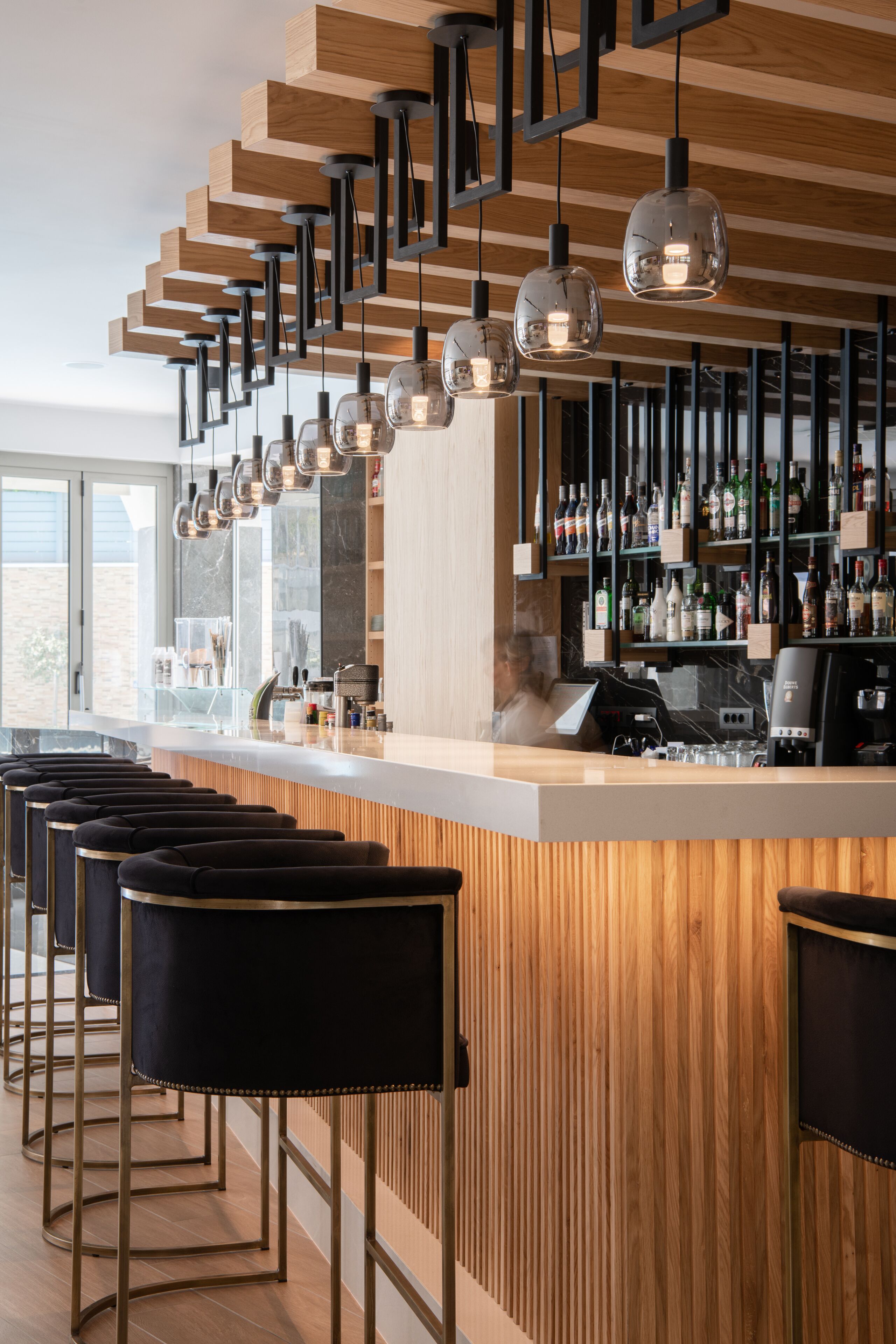 Un bar moderno con detalles de madera, taburetes negros y lámparas colgantes.