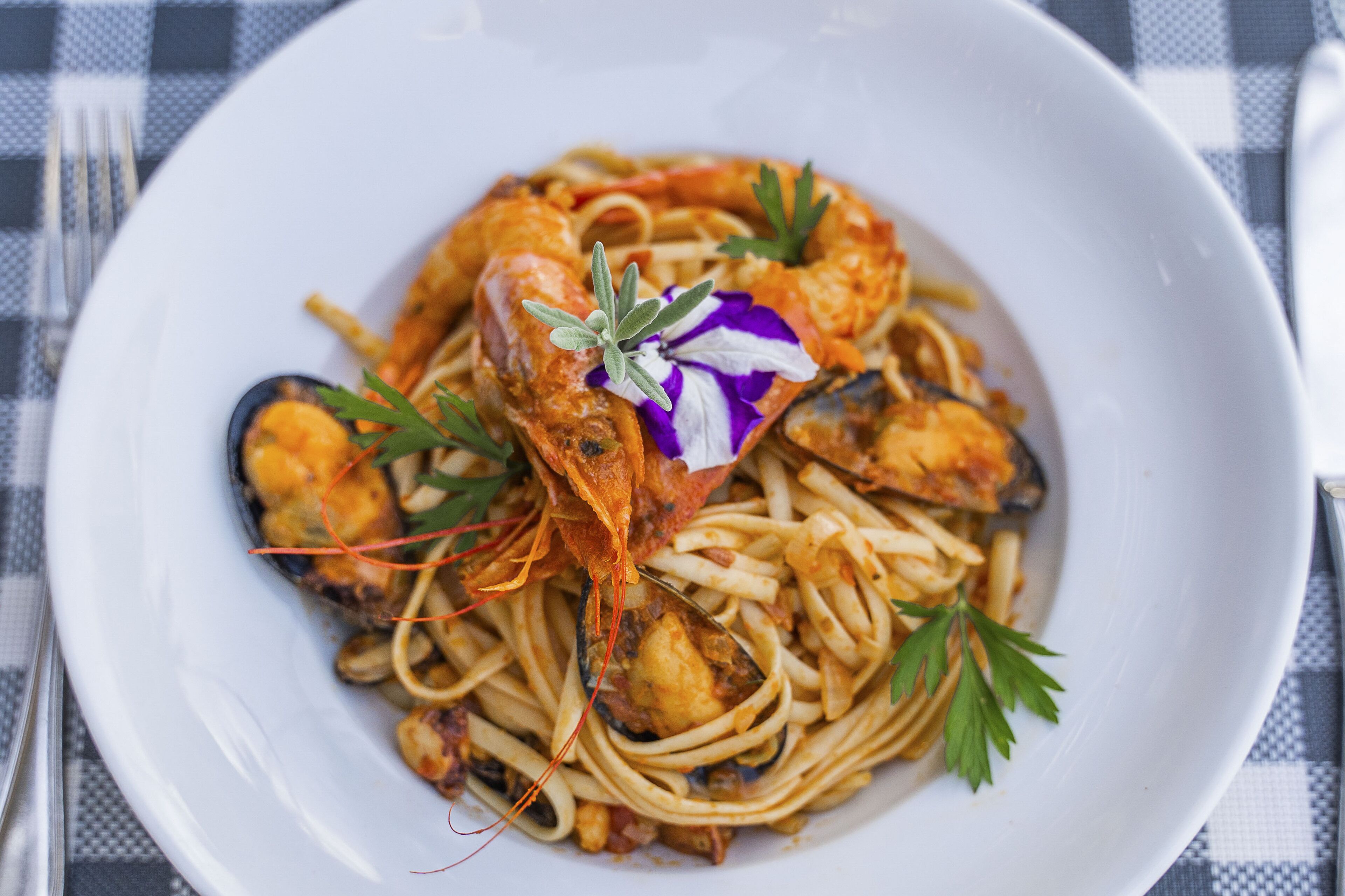Un plato de espagueti con mariscos, adornado con perejil y una flor morada.