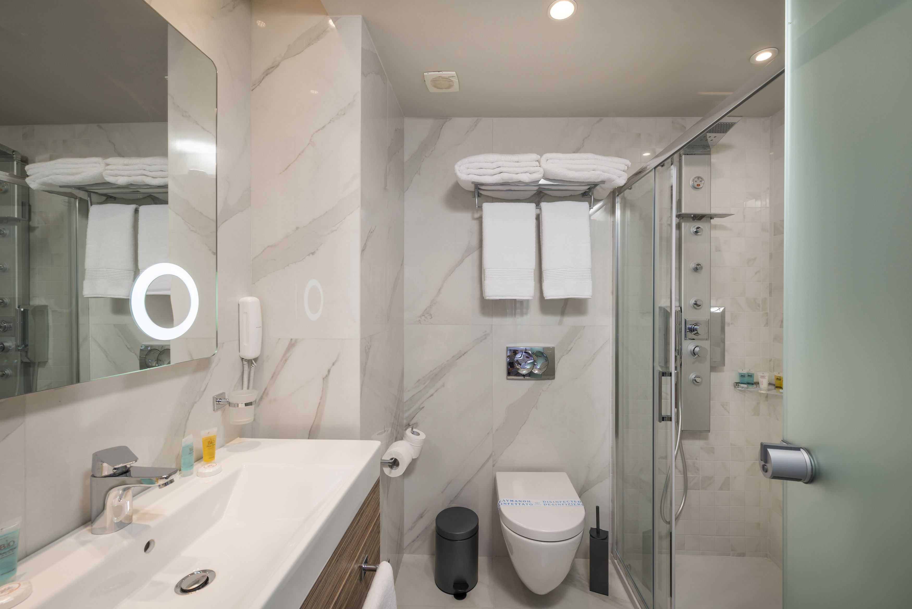 A modern bathroom with a marble sink, a glass shower enclosure, and a toilet with a towel rack above.