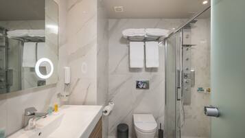 A modern bathroom with a marble sink, a glass shower enclosure, and a toilet with a towel rack above.