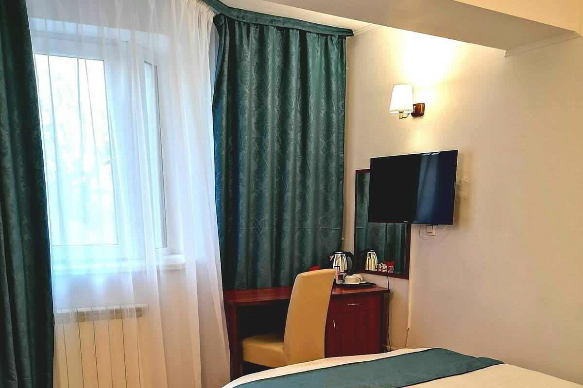 A hotel room with a bed, a desk, a chair, a TV, and a telephone.