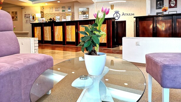 Un hall de hotel con una mesa de recepción, una planta en maceta y dos sillones morados.