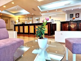Un hall de hotel con una mesa de recepción, una planta en maceta y dos sillones morados.