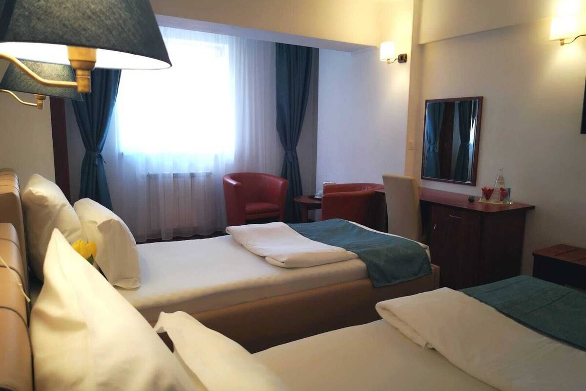 A hotel room with two beds, a desk, a chair, a mirror, and a lamp.