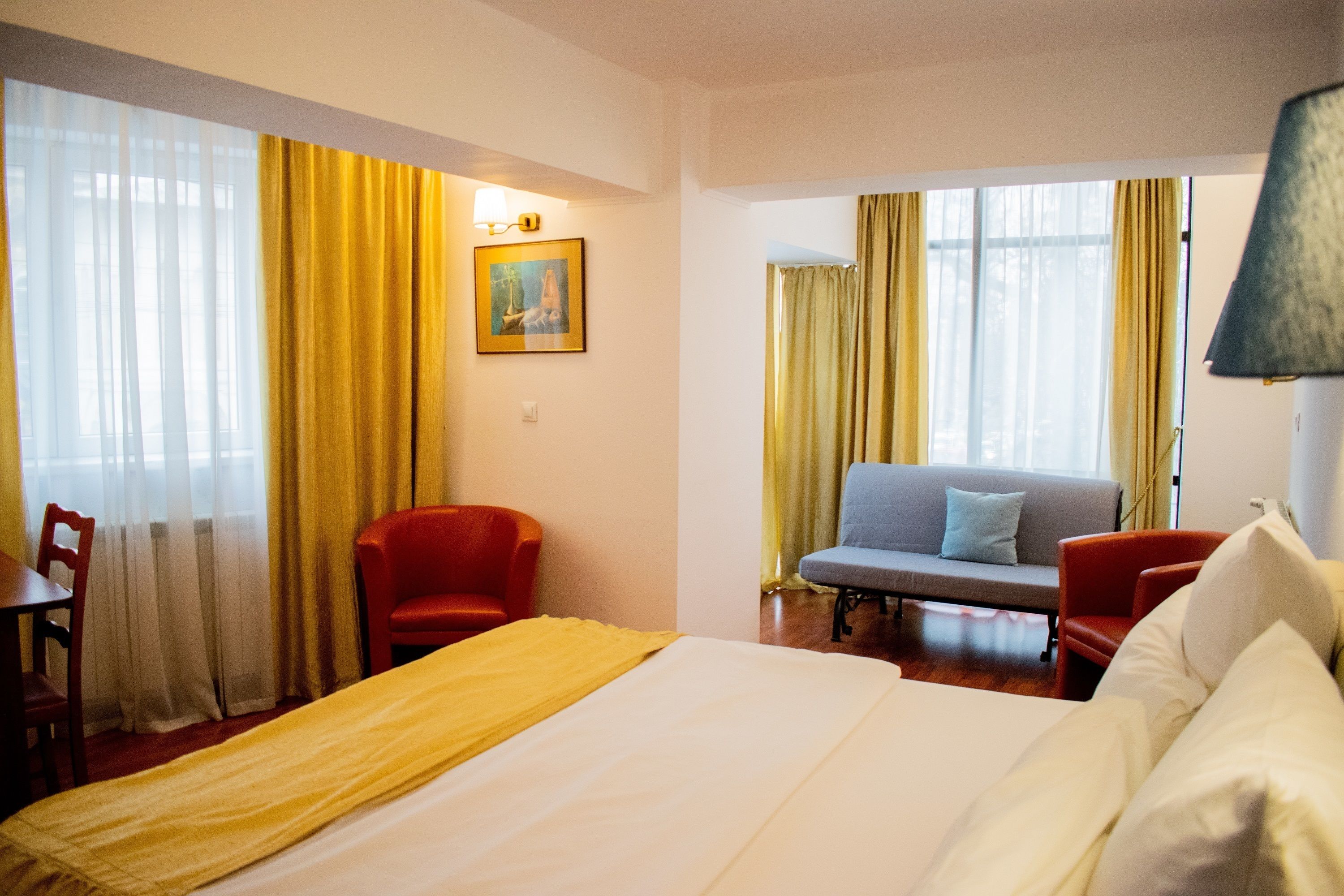 Una habitación de hotel con una cama, dos sillas, un sofá y un cuadro en la pared.