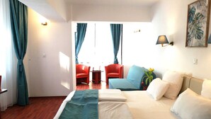 Habitación de hotel con cama, sofá, dos sillones, una mesita y un cuadro en la pared.