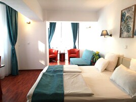Habitación de hotel con cama, sofá, dos sillones, una mesita y un cuadro en la pared.