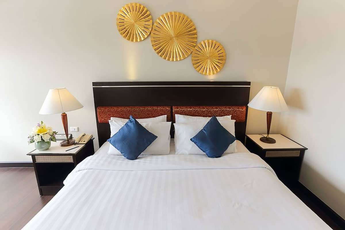 A hotel room with a large bed, two bedside tables with lamps, a decorative wall piece, and a vase with flowers.