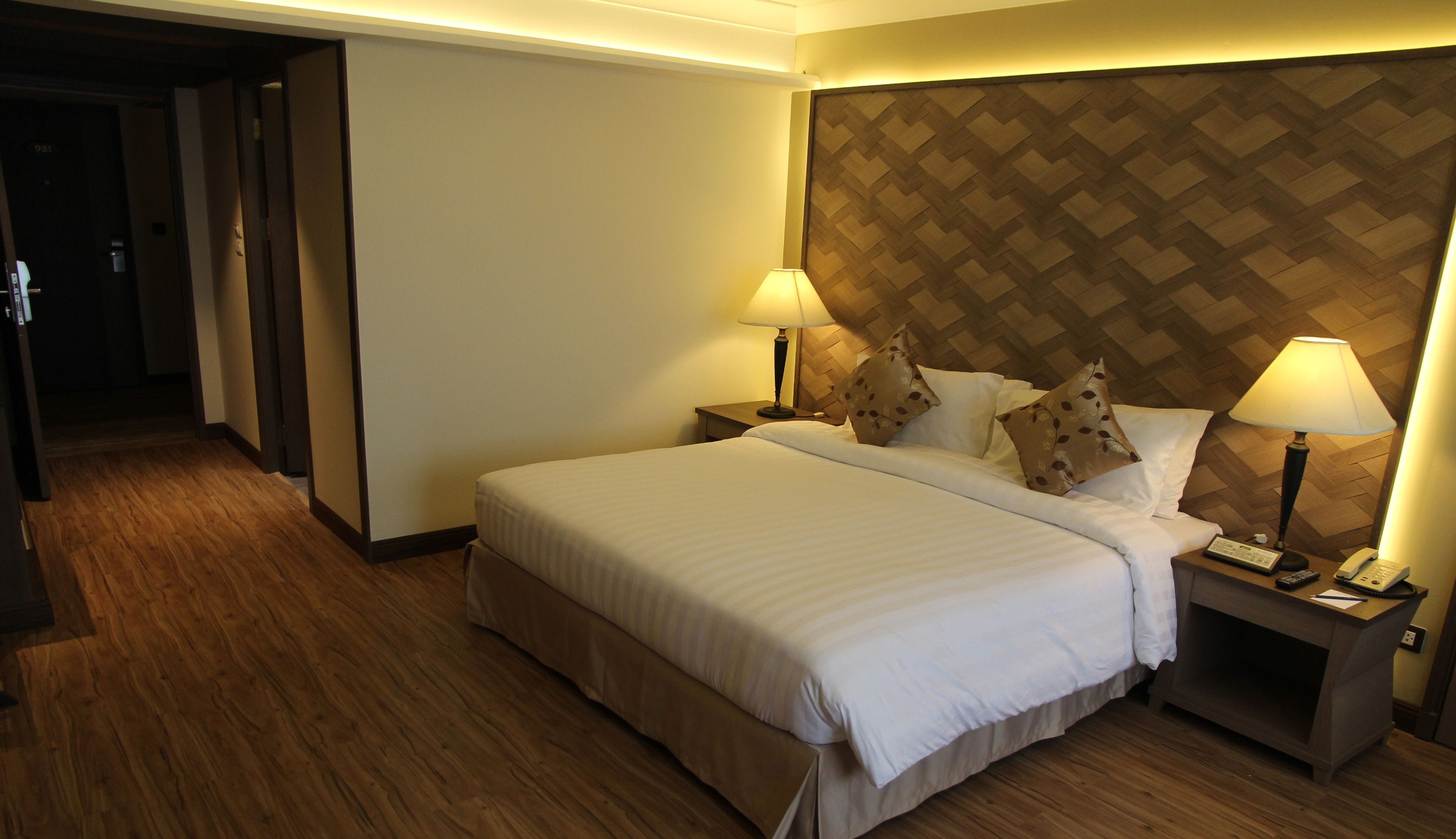 Una habitación de hotel con una cama grande, dos mesitas de noche con lámparas, un cabecero de madera y suelo de madera.