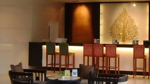 A lobby with a reception desk, several chairs, a round table, and a decorative wall piece. - Amora Hotel Tapae Chiang Mai (Chiang Mai)