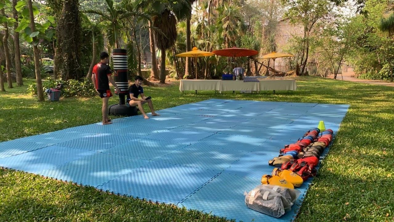 A blue mat laid out on grass with a table and umbrellas in the background.