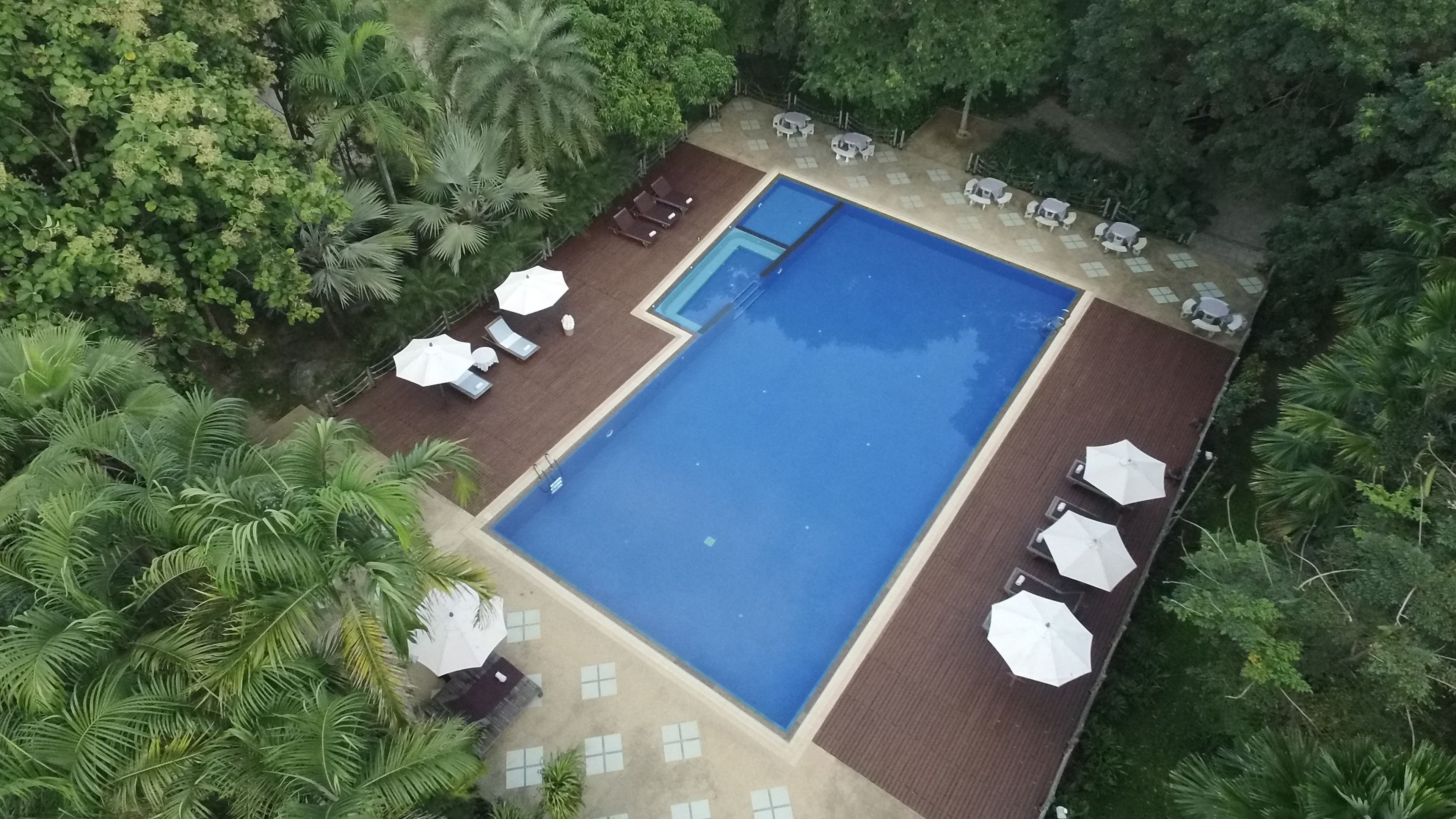 A rectangular swimming pool with a wooden deck, surrounded by white umbrellas and lounge chairs.