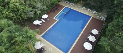 A rectangular swimming pool with a wooden deck, surrounded by white umbrellas and lounge chairs.