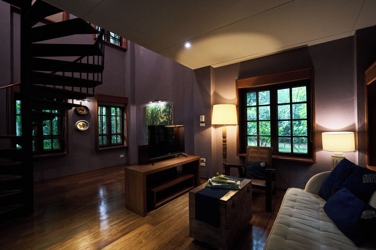 Une pièce avec un escalier en bois, une télévision, une lampe, un canapé et une fenêtre donnant sur un paysage verdoyant.