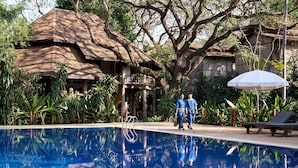 A pool area with a thatched-roof structure, a lounge chair, and a hanging umbrella. - Kaomai Lanna Resort (San Pa Thong)